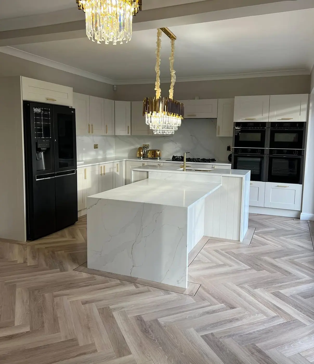 White kitchen with waterfall island, crystal chandelier and American fridge freezer